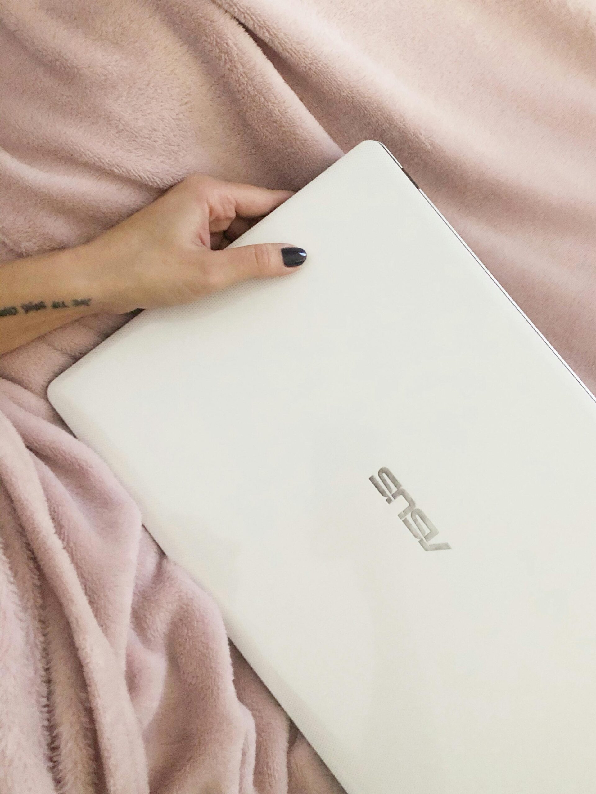 Close-up of a hand holding a white laptop on a soft pink blanket.